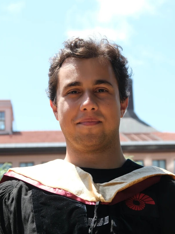 Portrait of Tolga Recep Ucar in academic regalia, outdoors in front of a brick building