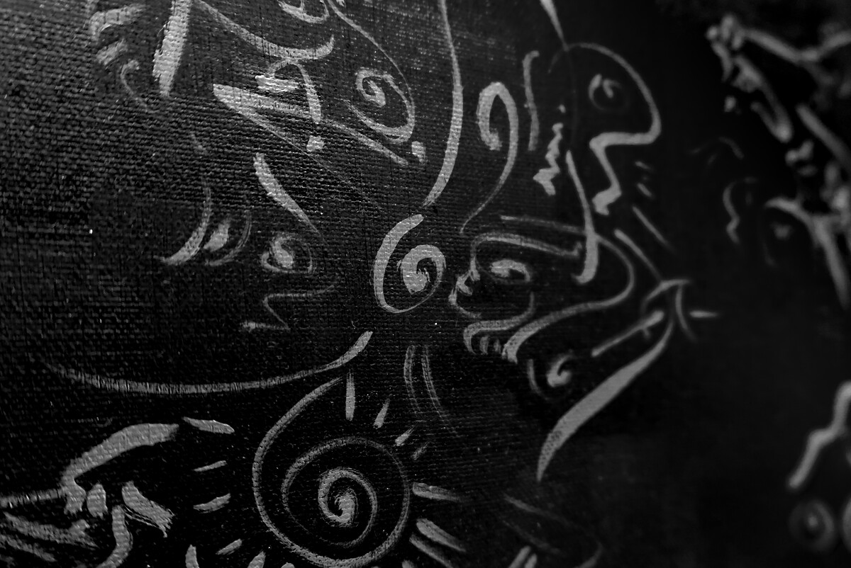 Close-up, in black and white, of silver line drawings of faces and spirals on dark canvas